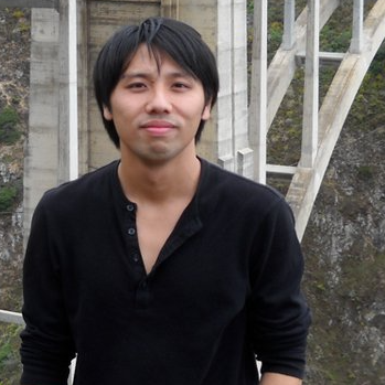 Lok in a black shirt standing in front of a large concrete bridge. The background features a rocky landscape visible through the bridge's arches.